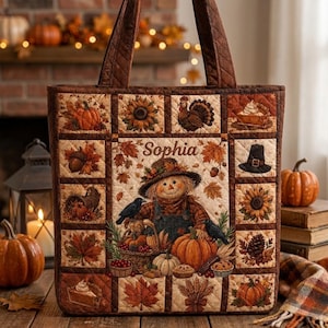 Op de afbeelding: Een gewatteerde draagtas met een patchworkontwerp met herfstthema's, waaronder pompoenen, zonnebloemen, een kalkoen, een pelgrimshoed en een centrale vogelverschrikker-afbeelding met de naam Sophia in bruine schrijfletters.