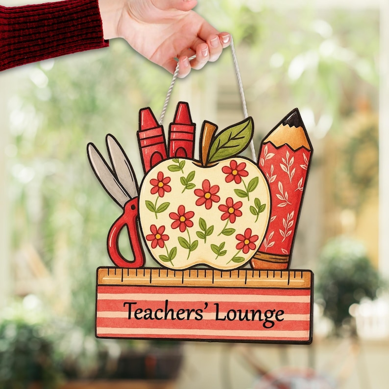 May include: A wooden sign with a white string for hanging, featuring school supplies. The design includes red crayons, scissors, a pencil, and an apple decorated with red flowers. The sign reads "Teachers' Lounge" in black text on a ruler.