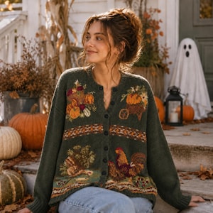 May include: A dark olive green button-down cardigan featuring a knit pattern of autumn harvest motifs, including pumpkins, a cornucopia, a turkey, and a rooster. The garment has long sleeves, a crew neckline, and a row of dark buttons down the front.