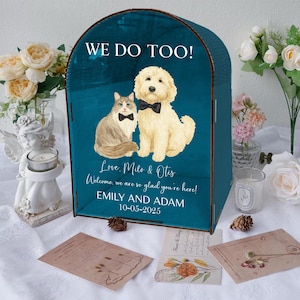 Op de afbeelding: Een teal houten kaartenbox met de tekst "WE DO TOO!" en een aquarel illustratie van een kat en een hond met vlinderdassen. De box bevat de namen "EMILY AND ADAM" en de datum "10-05-2025".
