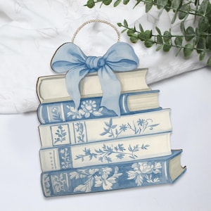 Può includere: Ornamento in legno a forma di pila di libri blu e bianchi, decorati con motivi floreali. Un fiocco azzurro chiaro è legato in cima, con un anello di spago per appendere. Il design evoca uno stile vintage e country, ideale per l'arredamento della casa.