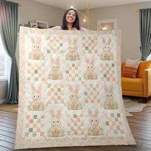 May include: A quilted blanket featuring a repeating pattern of Easter bunnies holding baskets of eggs. The bunnies are in a soft, pastel color palette, set against a patchwork background of squares in similar hues. The blanket has a floral border.