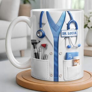 May include: A white ceramic mug featuring a graphic of a doctor's white coat over blue scrubs. The design includes a blue stethoscope, a name tag reading DR. LUCIA, a reflex hammer, a penlight, a prescription pad, and a bottle of pills.