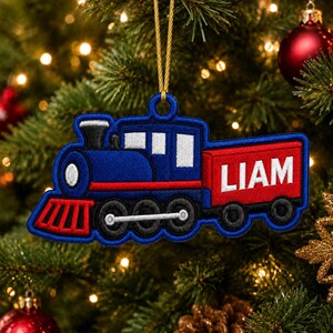 May include: A blue and red embroidered train ornament featuring the name LIAM in white capital letters on the side. The train has black wheels, a white headlight, and a gold hanging cord attached to the top loop for display on a tree.