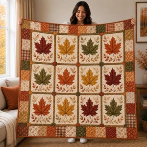 Pode incluir: Uma colcha quadrada com uma grelha de doze blocos, cada um exibindo uma grande folha de ácer em tons de vermelho, laranja, amarelo e verde sobre um fundo creme, rodeada por uma borda de quadrados de patchwork mais pequenos em cores outonais.