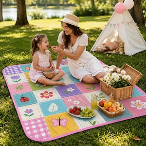 May include: A rectangular picnic blanket featuring a patchwork design of colorful squares with patterns of flowers, butterflies, ladybugs, leaves, and pink gingham. The blanket is spread on grass and holds a wicker basket and a plate of fruit.