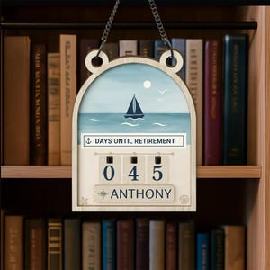 May include: A wooden retirement countdown plaque with a nautical theme. The plaque features a watercolor painting of a sailboat on the sea, with the text "DAYS UNTIL RETIREMENT". The counter displays "045" days. The name "ANTHONY" is printed below the counter.