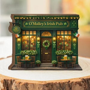 May include: A miniature wooden replica of O'Malley's Irish Pub. The facade is painted dark green with gold accents, featuring a sign, Irish flags, and a wreath. Tables and chairs are set outside, with a beer on each table. The pub's name is displayed.