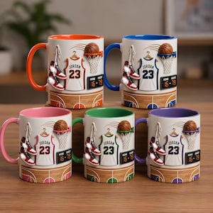 Puede incluir: Cinco tazas de cerámica con diseños de baloncesto. Cada taza presenta una pelota de baloncesto, una camiseta con "Jordan 23", zapatillas y un marcador. Las tazas tienen asas y bordes interiores de diferentes colores: naranja, azul, rosa, verde y morado.