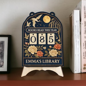 May include: A navy blue wooden book counter with the text "BOOKS READ THIS YEAR" and "EMMA'S LIBRARY". The counter shows "085" with floral and bird illustrations. The design includes a full moon and a wooden stand.