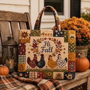 Puede incluir: Un bolso tote acolchado con un borde de patchwork en colores otoñales y un panel central con el texto Hi Fall rodeado por una corona de hojas y cuatro gallinas. El bolso tiene dos asas acolchadas a juego y un patrón de costura de diamantes.