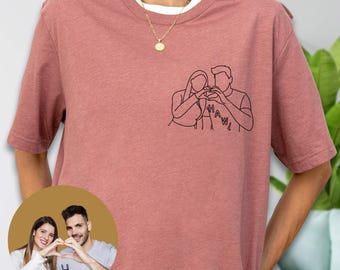 May include: A dusty rose short-sleeve t-shirt featuring a black line art illustration on the left chest. The graphic depicts two people forming a heart shape with their hands, with the word HAWL printed below the figures in a simple black font.