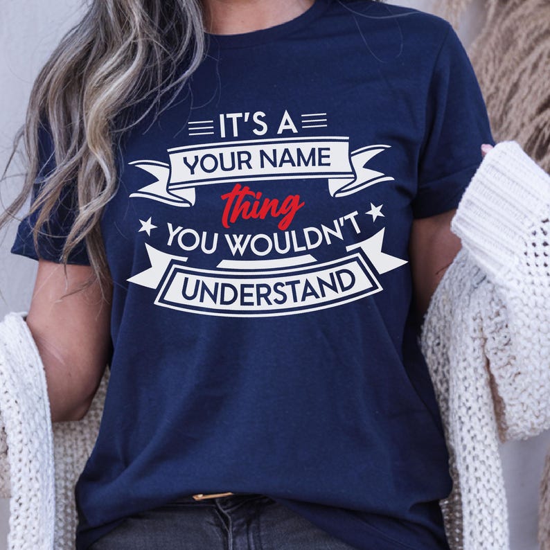 May include: A navy blue short-sleeved t-shirt featuring white and red graphic text that reads IT'S A YOUR NAME thing YOU WOULDN'T UNDERSTAND, arranged with decorative banners and stars across the chest area of the garment.