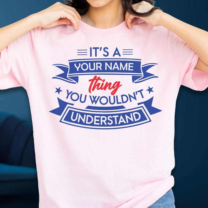 May include: A light pink t-shirt featuring blue and red text that reads: IT'S A YOUR NAME thing YOU WOULDN'T UNDERSTAND. The design includes blue banners, stars, and horizontal lines, with the word thing written in a red script font.