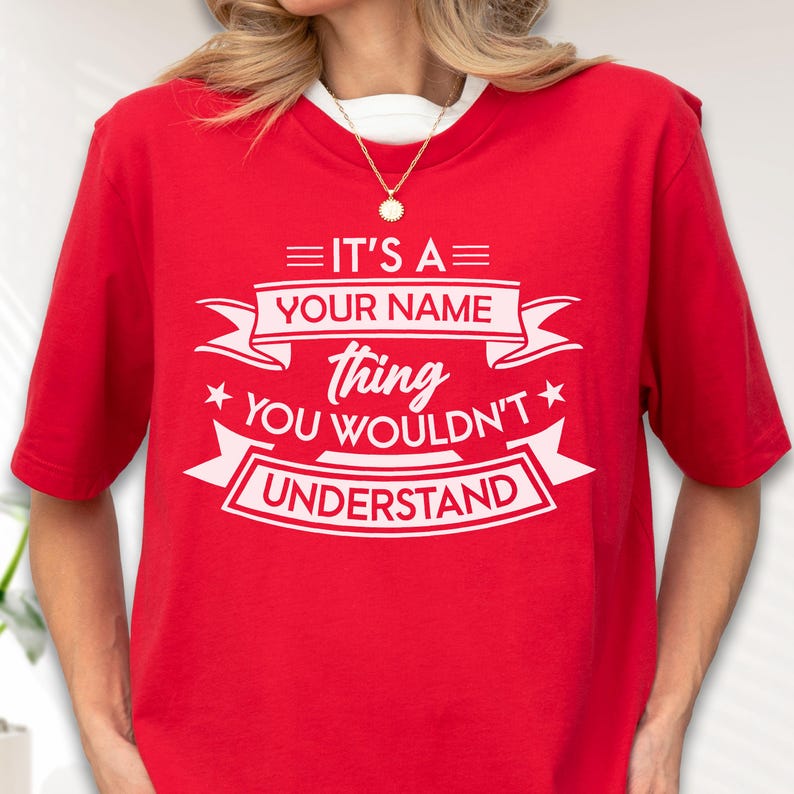 May include: A bright red short-sleeved t-shirt featuring white text that reads: IT'S A YOUR NAME thing YOU WOULDN'T UNDERSTAND, framed by decorative banners and stars. The design is centered on the chest of the shirt, which has a crew neckline.