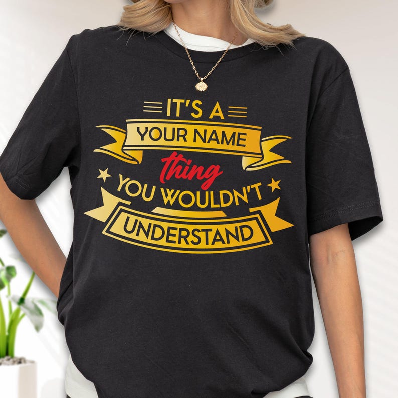 May include: A black short-sleeved t-shirt featuring yellow and red graphic text that reads IT'S A YOUR NAME thing YOU WOULDN'T UNDERSTAND, arranged within decorative yellow banners and accented with small yellow stars on the front chest area.