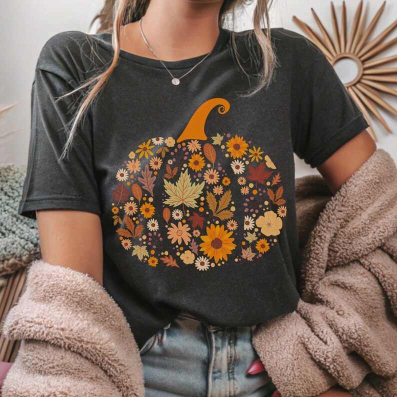 May include: Dark gray t-shirt featuring a floral pumpkin design. The pumpkin is filled with various autumn-colored flowers and leaves, including sunflowers, maple leaves, and daisies. The pumpkin has an orange stem. The shirt is a casual, short-sleeved style.