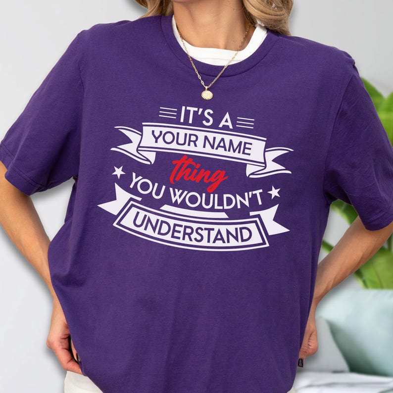 May include: A purple short-sleeved t-shirt featuring white and red text that reads IT'S A YOUR NAME thing YOU WOULDN'T UNDERSTAND, arranged within decorative banner elements and stars on the front of the garment.