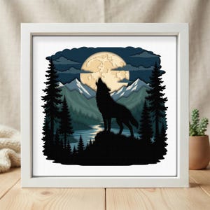 May include: A square white frame containing a layered paper art piece depicting a black silhouette of a wolf howling at a large pale yellow moon. The scene includes dark evergreen trees, blue mountain peaks, and a reflective river under a night sky.