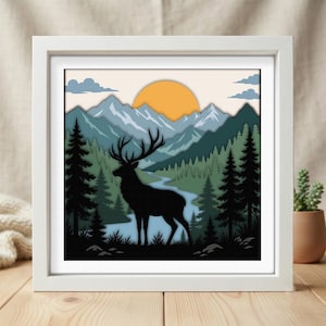 Puede incluir: Una pieza de arte mural cuadrada enmarcada con un diseño de papel recortado en capas que muestra la silueta negra de un ciervo en un bosque. El fondo presenta un río azul serpenteante, pinos verdes, montañas azules y un gran sol naranja.