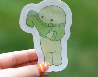 May include: A die-cut sticker featuring a cartoon figure pulling a green sweater over its head. The figure is light green with a simple face, and the sweater is a darker shade of green. The sticker has a white border.