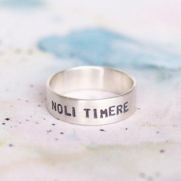 May include: A silver band ring with the words "NOLI TIMERE" engraved on it.