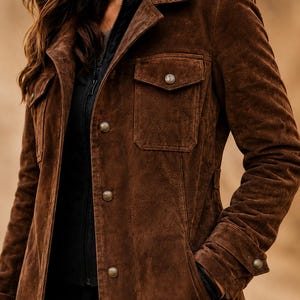 May include: A dark brown suede jacket featuring a collared neckline, long sleeves with buttoned cuffs, and two chest pockets with buttoned flaps. The front closure consists of a series of round metallic buttons, layered over a black zippered garment.