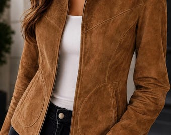 May include: A brown suede jacket featuring a full-length front zipper, a classic collar, and two rounded front pockets. The jacket is worn over a white tank top and black jeans, showcasing a fitted silhouette with structured seam detailing.