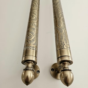 May include: Two antique bronze door handles with intricate floral and scrollwork patterns. The handles have a cylindrical shape with decorative end pieces and circular mounting plates. The metal has a warm, aged patina, suggesting a vintage or handcrafted origin.