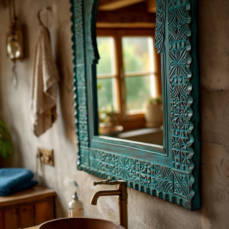 May include: A teal-colored, carved wooden mirror with intricate floral and geometric patterns. The mirror is rectangular with a decorative frame and is mounted on a textured wall. A brass faucet is visible below the mirror.