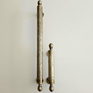 May include: Two antique brass door handles with an ornate paisley design. The larger handle is approximately 24 inches long, and the smaller handle is about 8 inches long. Both handles have a rounded top and bottom.