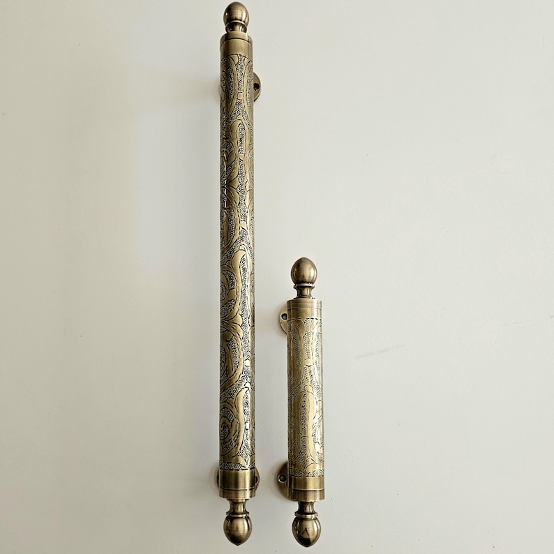 May include: Two antique brass door handles with an ornate paisley design. The larger handle is approximately 24 inches long, and the smaller handle is about 8 inches long. Both handles have a rounded top and bottom.