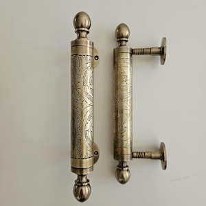 May include: Two antique bronze door handles. Each handle features intricate floral patterns and a rounded top and bottom. One handle has a side mount. The handles are approximately 10 inches in length.