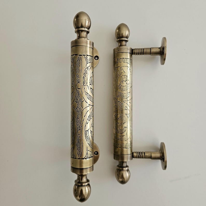 May include: Two antique bronze door handles. Each handle features intricate floral patterns and a rounded top and bottom. One handle has a side mount. The handles are approximately 10 inches in length.