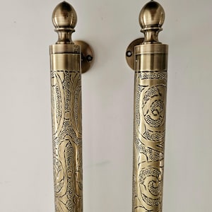 May include: Two antique brass door handles with ornate floral and swirl patterns. Each handle has a cylindrical body with detailed engravings and a rounded top. The handles are mounted on circular backplates.