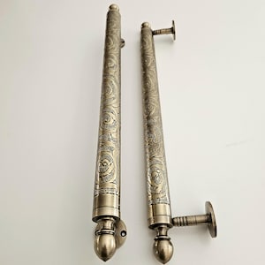 May include: Two antique bronze door handles with intricate floral scrollwork. The handles are cylindrical with decorative end pieces and mounting plates. One handle has a perpendicular grip. The handles are displayed against a white background.