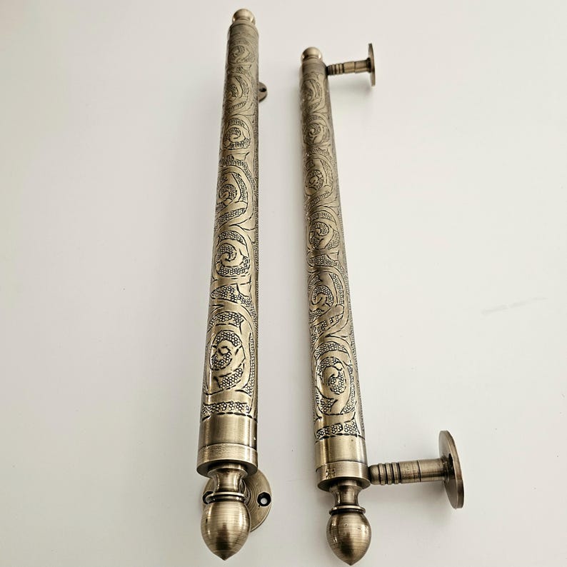 May include: Two antique bronze door handles with intricate floral scrollwork. The handles are cylindrical with decorative end pieces and mounting plates. One handle has a perpendicular grip. The handles are displayed against a white background.