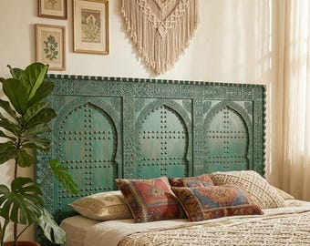 May include: A teal-colored, carved wooden headboard with arched panels and studded details. The bed is adorned with patterned pillows and a cream-colored, fringed throw. A macrame wall hanging and framed botanical prints complete the bohemian bedroom decor.