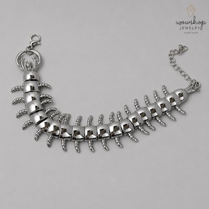 May include: A silver-toned metal bracelet shaped like a centipede with a segmented body, multiple small legs, and a detailed head. The bracelet features a lobster claw clasp and an adjustable chain link extension. The text wowshop JEWELRY HAND MADE is visible in the top right corner.