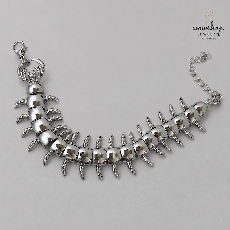 May include: A silver-toned metal bracelet shaped like a centipede with segmented body parts and multiple small legs extending from each side. The piece features a lobster claw clasp at one end and an adjustable chain link extension at the other.