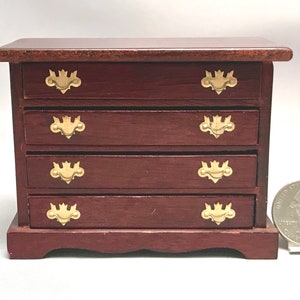 May include: A miniature wooden dresser with four drawers and gold-colored hardware. The dresser is about the size of a quarter.