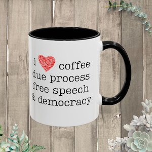 May include: White ceramic mug with a black interior and handle. The mug displays the text "I ❤️ coffee due process free speech & democracy" in black, with a red heart symbol.