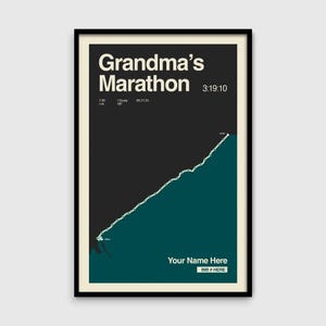 May include: Framed poster with the text "Grandma's Marathon" and a teal and white line graph. The poster includes the time 3:19:10, and the text "Your Name Here" and "BIB # HERE". The background is black and cream.