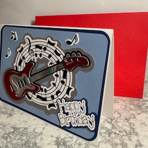 May include: A set of three ceramic mugs with a speckled, cream-colored glaze. Each mug features a different hand-painted design: a blue and green leaf, a yellow flower, and a red berry. The mugs have a simple, rounded shape.