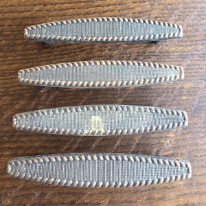 May include: Four antique bronze-toned drawer pulls. Each pull has a rectangular shape with a textured center and a rope-like border. The pulls are arranged on a wooden surface.