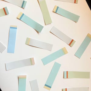 May include: An overhead shot shows several rectangular sticky notes scattered on a white surface. The notes are various pastel colors, including blue, green, and white, with colorful accent stripes. The notes are arranged at different angles.