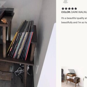 May include: A dark walnut record player stand with two tiers. The top tier holds a record player with a clear cover, while the bottom tier features a dedicated section for vertical vinyl record storage. The stand has four wooden legs.