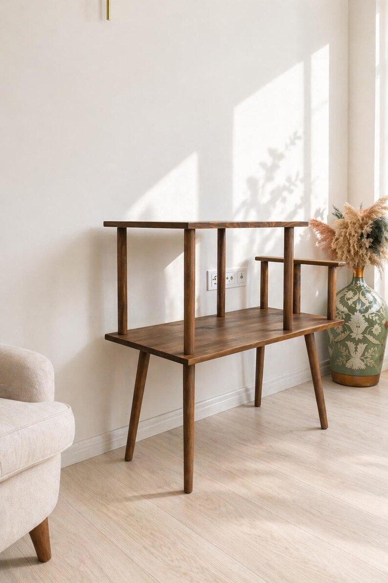 May include: A dark brown wooden tiered side table featuring a rectangular lower surface supported by four tapered legs and a smaller rectangular upper shelf held by four cylindrical posts, with an additional small side arm extending from the top.