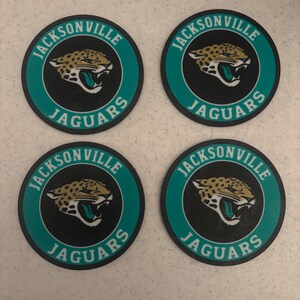 May include: Four circular coasters featuring the Jacksonville Jaguars logo. Each coaster has a black center with a jaguar head graphic, surrounded by a teal border with the text Jacksonville Jaguars printed in white lettering.