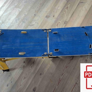 May include: A foldable blue wooden laptop desk with yellow legs. The desk is split into two sections and has several cut-out handles. The desk is designed to be portable and easy to store. The desk is on a wooden floor.